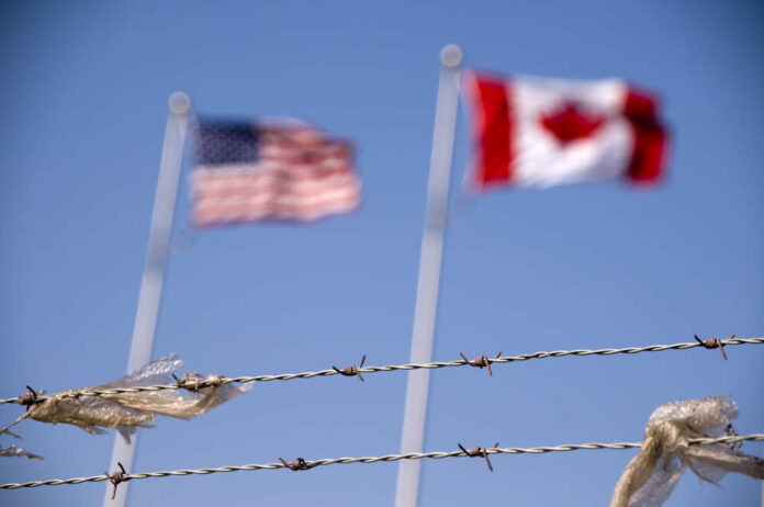 American,And,Canadian,Flags,Fly,Behind,Barbed,Wire
