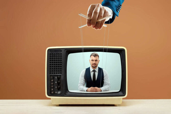 1991660915 Hand controlling puppet strings on TV broadcast