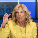 A woman in a yellow blazer speaking passionately during a meeting