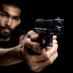 A man aiming a gun towards the camera against a dark background