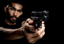 A man aiming a gun towards the camera against a dark background