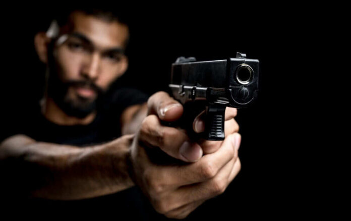 A man aiming a gun towards the camera against a dark background