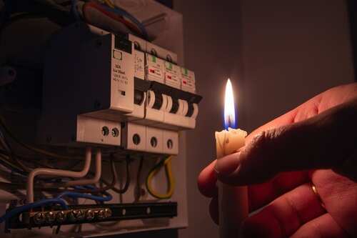 shutterstock_2117923766.jpg A hand holding a lit candle near an electrical panel