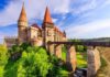 A medieval castle with tall towers and a wooden bridge surrounded by greenery