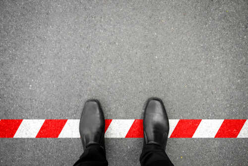 Person standing in black shoes at a red and white caution line on the ground