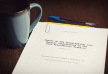 A printed report on a wooden desk next to a coffee mug and a pen