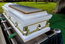 A white coffin placed on a green cloth at a cemetery