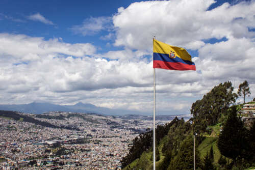 Ecuadorian flag waving over a city with mountains in the background