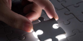 A hand placing a puzzle piece into a lit section of a puzzle