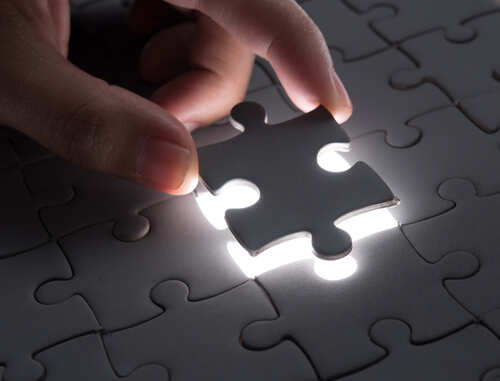 shutterstock_1674380023.jpg A hand placing a puzzle piece into a lit section of a puzzle