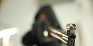 Close-up of a gun being aimed by a hooded figure