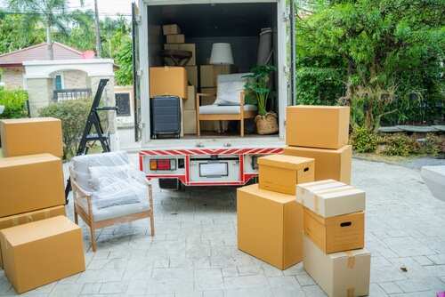 shutterstock_2300484823 (2).jpg A moving truck with furniture and boxes parked outside a house