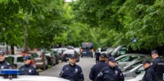 Group of police officers gathered on a street near parked cars