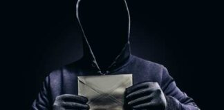 A hooded figure holding an envelope against a dark background