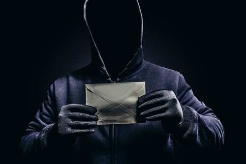 A hooded figure holding an envelope against a dark background