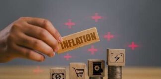 Hand placing a block labeled 'INFLATION' among stacks of coins and blocks with financial symbols