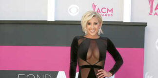 A woman in a black gown poses on the red carpet at an awards ceremony