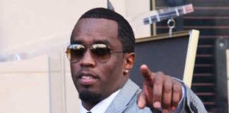 A man in a gray suit and sunglasses pointing towards the camera