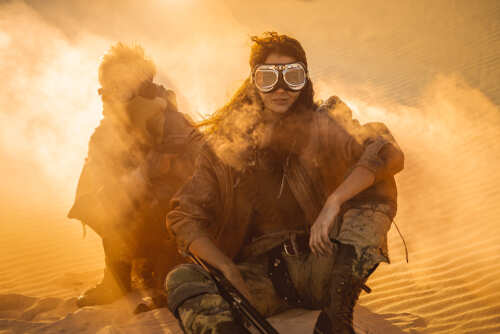 shutterstock_1635353662.jpg Two figures in a desert setting, one seated with a weapon and goggles