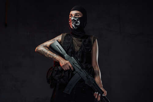 Individual in military attire holding a rifle against a dark background