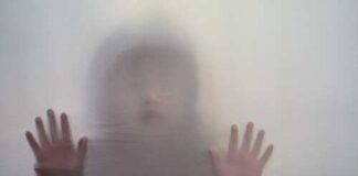 A blurred figure with hands pressed against a translucent surface