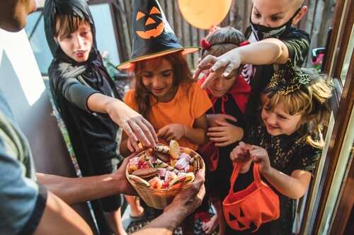 Children in Halloween costumes eagerly reaching for candy from a bowl