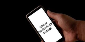 Hand holding a smartphone displaying the text 'Global Technology Outage'