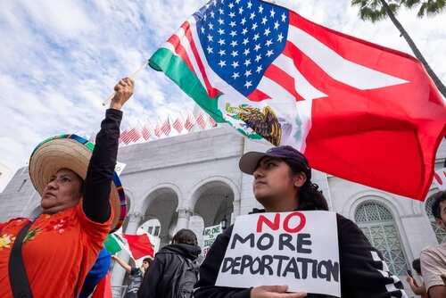 shutterstock_2583051845.jpg Two women at a protest holding flags and a sign against deportation