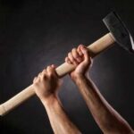 Hands gripping a large hammer against a dark background