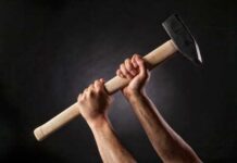 Hands gripping a large hammer against a dark background