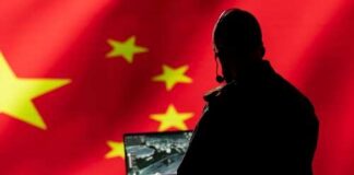 Silhouette of a military personnel operating a laptop in front of a Chinese flag