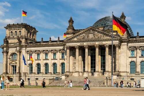The Reichstag building in Berlin with German flags and people walking in front