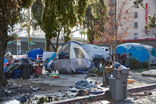 A homeless encampment with tents and scattered debris in an urban setting