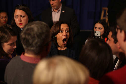 A woman with an expressive reaction surrounded by a crowd at a political event