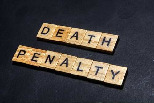 shutterstock_2389190169.jpg Wooden letter tiles spelling 'DEATH PENALTY' on a dark surface