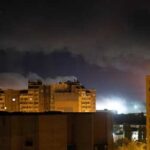 Nighttime view of urban buildings under a cloudy sky with distant lights