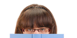 A girl with glasses peeking over a blue book