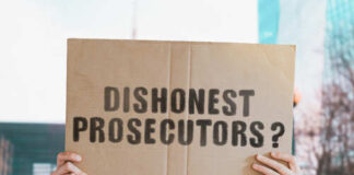 A person holding a cardboard sign that reads 'DISHONEST PROSECUTORS'