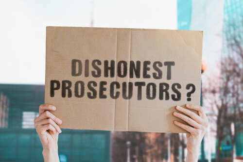 A person holding a cardboard sign that reads 'DISHONEST PROSECUTORS'