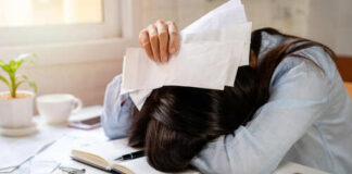 Person with head down on a desk surrounded by papers and credit cards