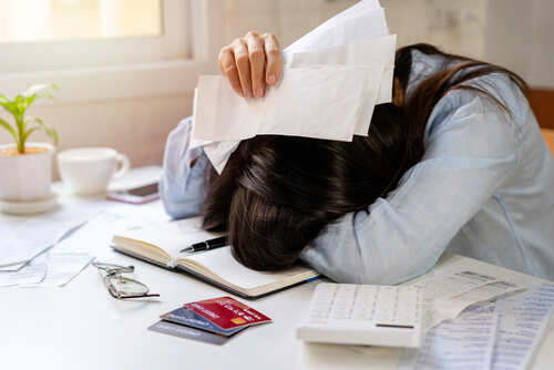 shutterstock_2011119128.jpg Person with head down on a desk surrounded by papers and credit cards