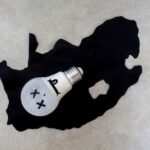 Tech Giants Drain Grid—Families Left In The Dark A light bulb with a face illustration placed on a black silhouette of South Africa