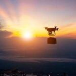 Drone flying against a sunset backdrop carrying a package