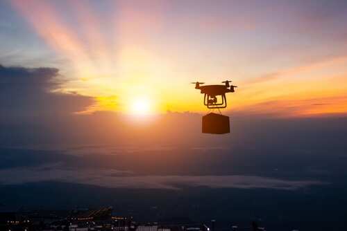 Drone flying against a sunset backdrop carrying a package
