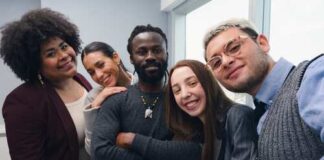 A diverse group of five people smiling together in an office setting