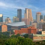 Trump’s Bold Move: Minneapolis Under Siege A panoramic view of a city skyline featuring modern skyscrapers and greenery in the foreground