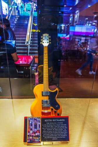 A vintage guitar displayed in a glass case with a plaque
