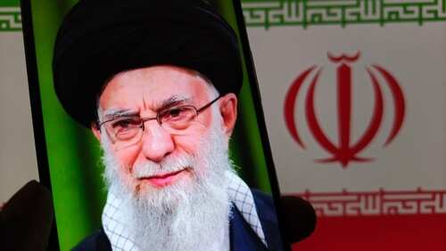 shutterstock_2641472919.jpg Close-up portrait of a political figure displayed on a smartphone with an Iranian flag background