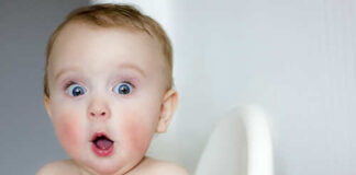 A surprised baby sitting in a high chair with wide eyes and an open mouth