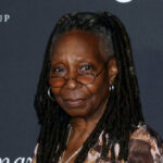 A smiling woman with dreadlocks wearing glasses at a red carpet event